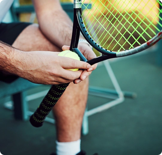 A close-up shot of a male tennis player sitting down, holding a tennis ball against the strings of his tennis racket.