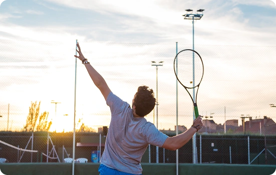A tennis player in a white uniform during a serve motion on an outdoor tennis court.